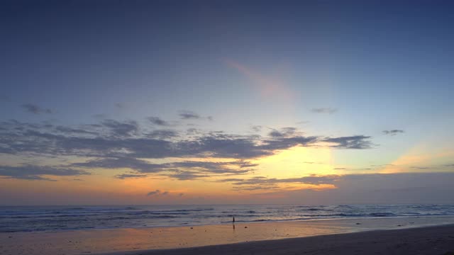 美丽的日落与渔民的剪影和彩色的天空在一个平静的海滩与黑色的沙子和波浪与雾视频下载