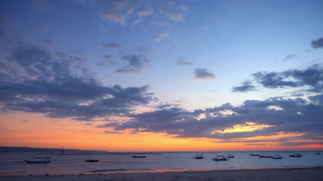 巴厘岛渔船的剪影，在热带泻湖与小低潮波缤纷的蓝色和橙色日落视频下载