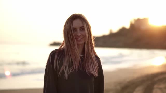 一个女人的肖像沿着海滩微笑着走，海边的黄昏的秋天视频素材
