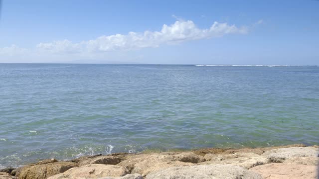 在阳光明媚的日子里，有肮脏的绿色水和礁石上的波浪的石头海滩视频下载