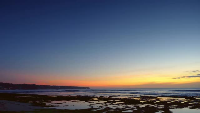 日落后的海滩，低潮时深蓝色和红色的天空，海浪在礁石和岩石上视频下载