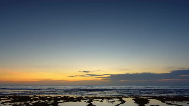 日落后的海洋全景与美丽的蓝色和黄色的天空在低潮与高波浪礁和岩石视频下载