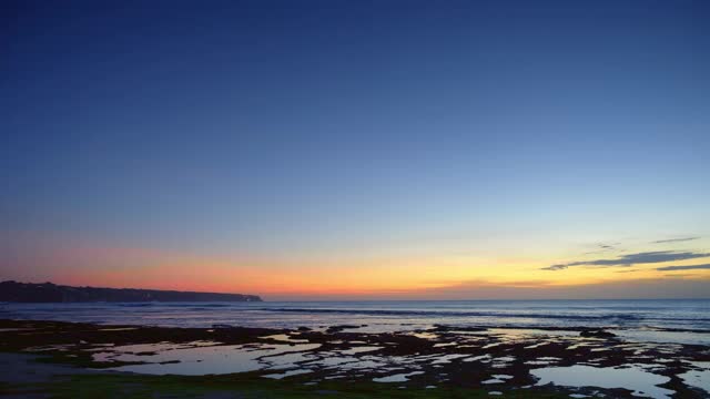 日落后的海滩，深蓝色的水、天空和岩石附近的海浪视频下载
