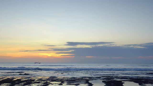 日落后的大海全景，礁石上有巨浪，背景是小船视频下载
