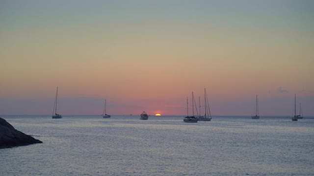 日落的最后几秒钟在平静的海湾与游艇和船的剪影与红色的太阳在地平线后面视频下载