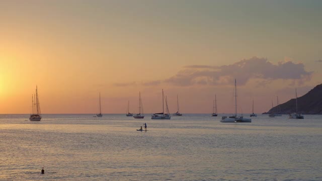 人们的剪影是在多彩的电影日落与蓝色和紫色的天空在热带海湾游艇和双体船视频下载