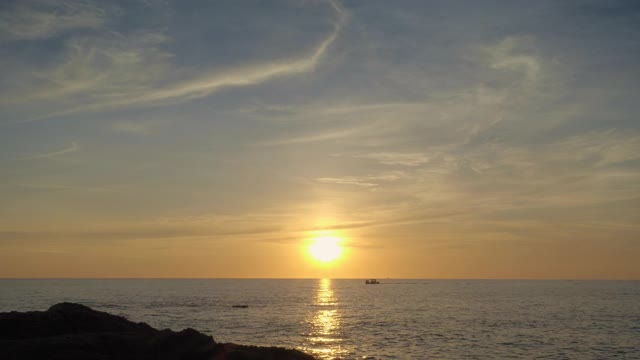 美丽的日落从岩石海滩与小船的剪影和太阳接近地平线视频下载