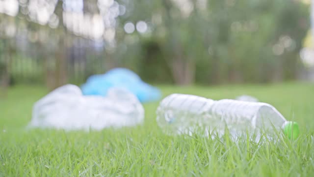 一个人把一个塑料瓶掉在公园的草地上。他破坏自然，增加塑料垃圾。4 k决议。视频素材
