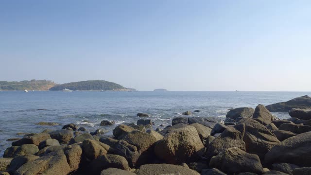 岩石海滩与波浪和水花和岛屿与山和船的背景视频下载