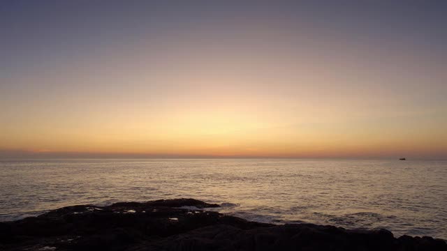 美丽多彩的日落从岩石海滩与深蓝色的天空和船的剪影接近地平线视频下载