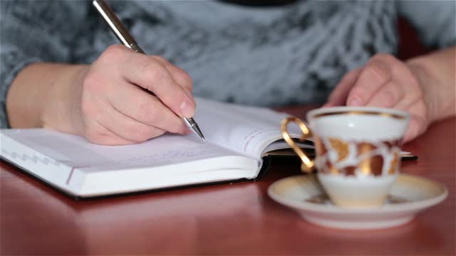 这个女人在笔记本上写字，喝着咖啡。视频下载