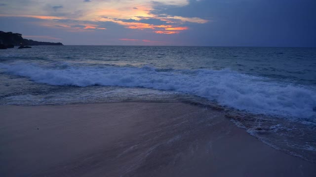 热带海滩在黑暗的夜晚与高浪潮附近的岩石和蓝色与橙色的日落天空视频下载