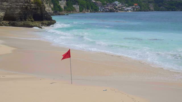炎热的天气里，热带海滩上的大浪正在缓慢地挤压沙子，海滩上挂着红色游泳禁止旗，海水中有塑料和有机垃圾视频下载