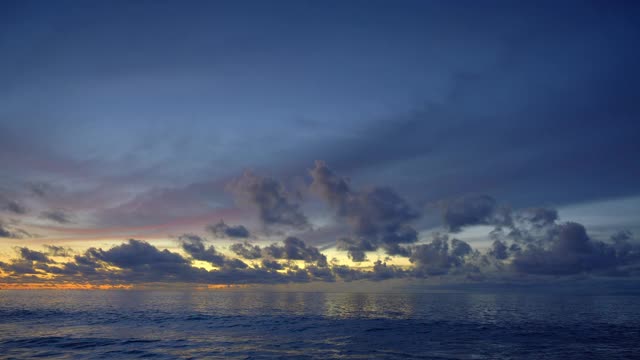 美丽的全景，一个平静的海与大的蓝色波浪附近的海滩日落后与云在黄色和紫色的天空反射在水视频下载