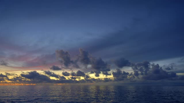 美丽的全景，一个平静的海与深蓝色的波浪日落后与云在黄色和紫色的天空反射在水视频下载