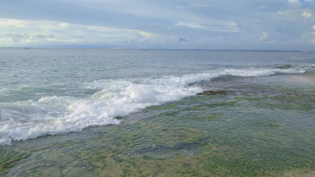 巨大的泡沫波浪在傍晚的海滩与绿色的海藻和蓝色的海洋背景视频下载