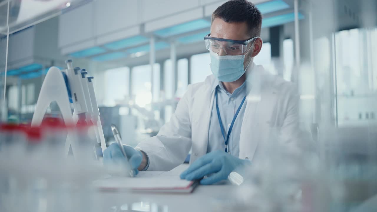 医学研究实验室:男性科学家戴着口罩看着相机，写下信息的肖像。医学、生物技术、微生物学发展先进科学实验室视频素材