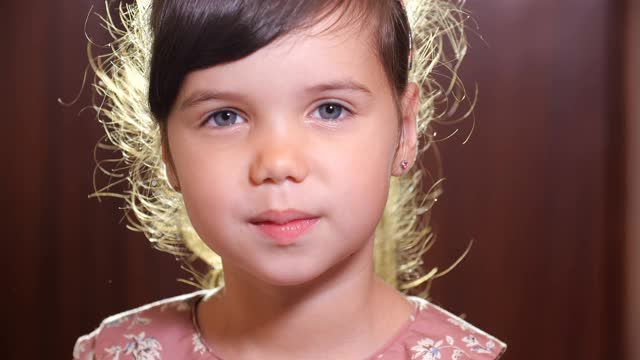 一个学龄前的小欧洲女孩的特写，棕色的头发和蓝色的眼睛在粉红色的衣服打喷嚏和擤她的鼻子用白色的手帕覆盖鼻子。4k 50fps慢动作视频素材