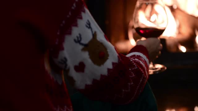 穿着圣诞毛衣的女人坐在壁炉旁，拿着一杯红酒视频下载