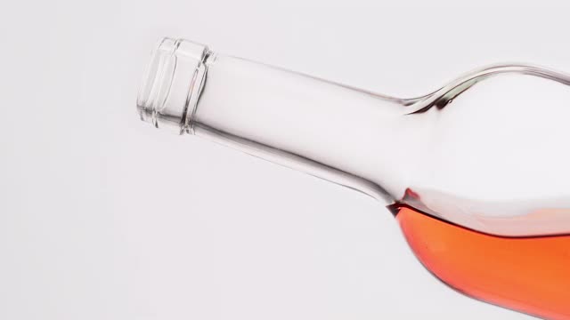 用慢动作从一个透明的瓶子里倒出玫瑰酒在白色的背景上视频素材