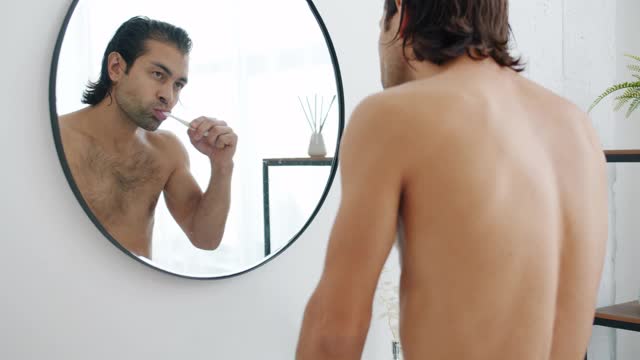一个年轻人在浴室里刷牙然后看着镜子的慢动作视频素材