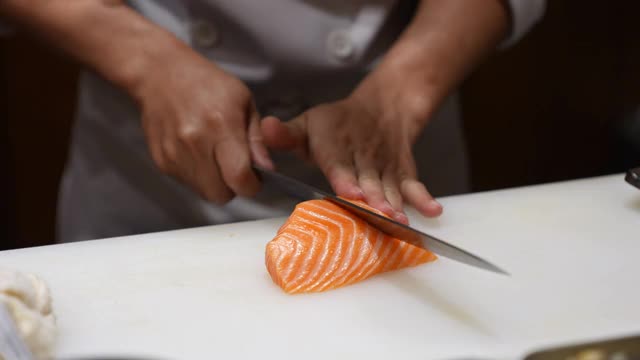 4K近距离拍摄专业男厨师手用鱼片刀在餐厅厨房的砧板上切鲜橙鲑鱼肉。厨师准备健康菜单，鲑鱼，生鱼片或寿司给顾客视频素材