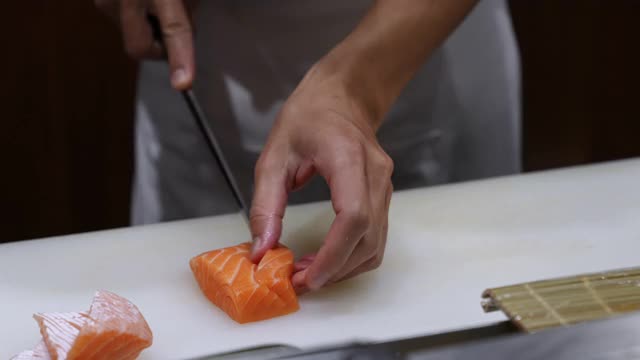 4K近距离拍摄专业男厨师手用鱼片刀在餐厅厨房的砧板上切鲜橙鲑鱼肉。厨师准备健康菜单，鲑鱼，生鱼片或寿司给顾客视频素材