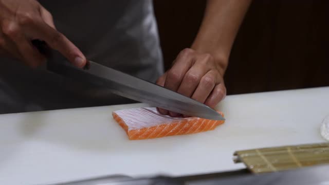 4K近距离的专业厨师手使用鱼片刀切新鲜的三文鱼肉在餐厅厨房砧板上。厨师为顾客准备健康菜单上的三文鱼饭团，生鱼片或寿司视频素材