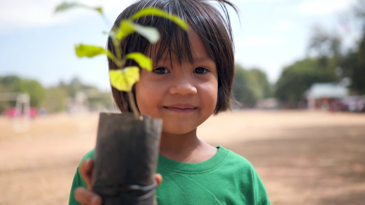 一个亚洲小女孩在春天的绿色背景下，手里拿着一株植物。视频下载