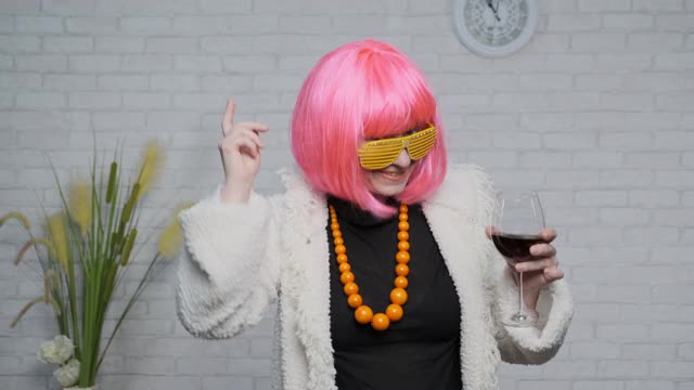 快乐的成年女子，粉红色的头发跳舞，手里拿着一杯酒庆祝成功视频下载