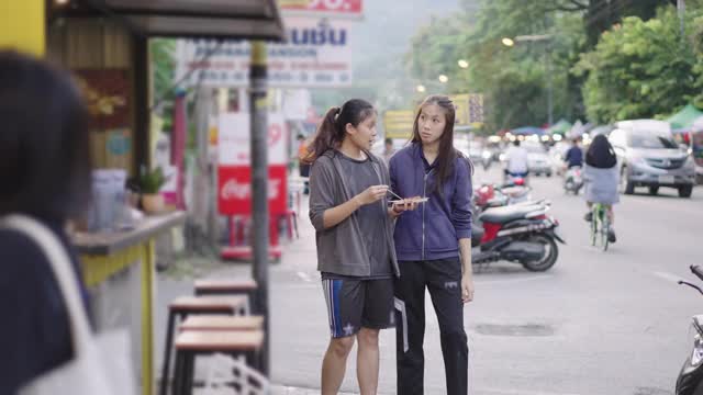 两个朋友喜欢在当地的街道上购物和吃饭，同时吃一些街头小吃视频下载