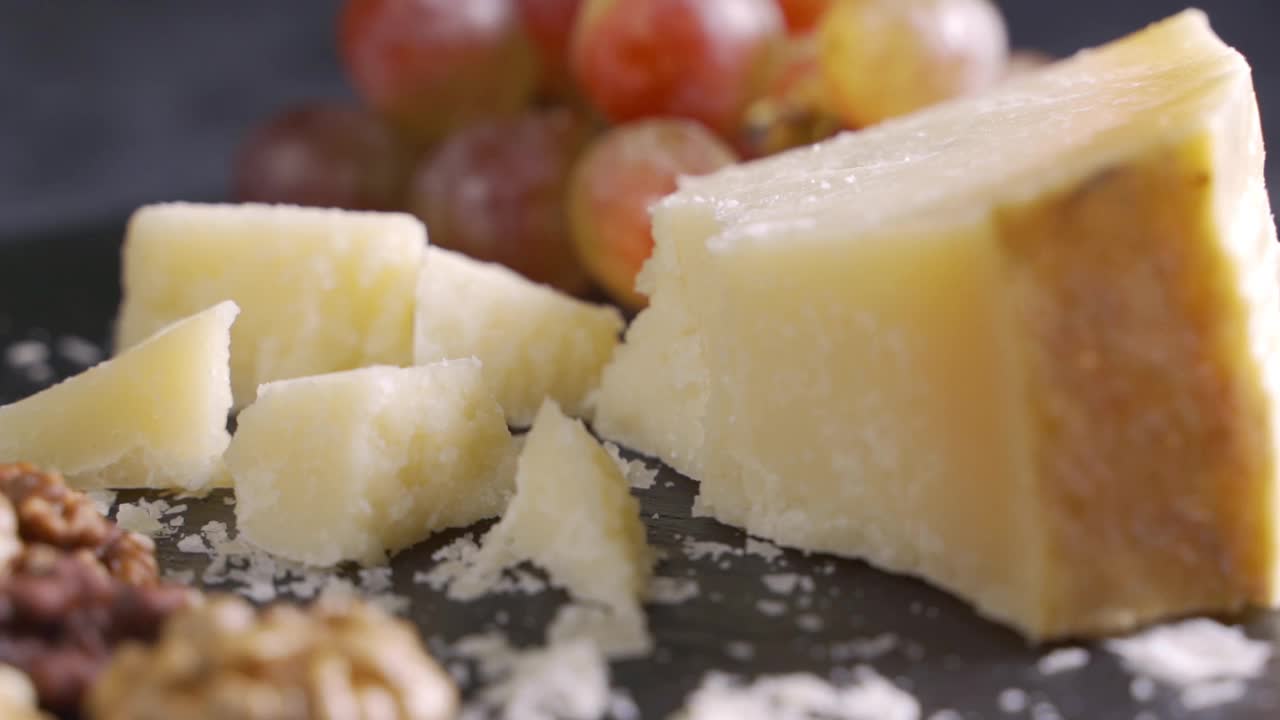 美味的帕玛森奶酪装在黑色的石头盘子里，配上核桃和葡萄。视频下载
