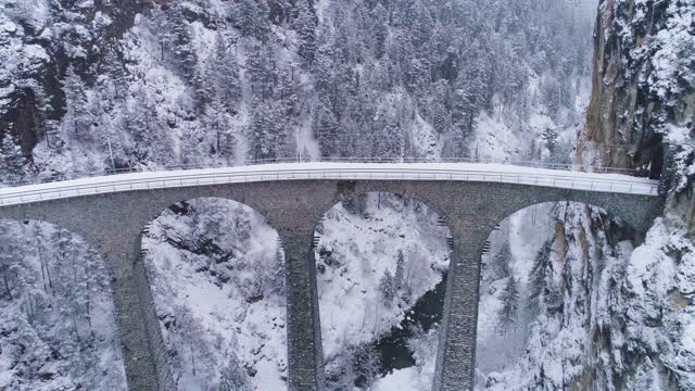 冬季有铁路和火车的Landwasser高架桥。下雪。瑞士阿尔卑斯山。瑞士。鸟瞰图。无人机向后和向上飞行。揭示拍摄视频素材