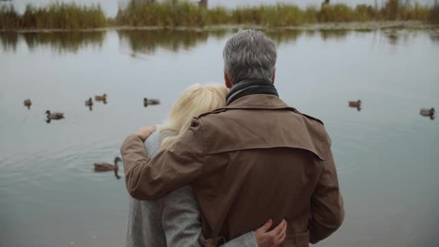 一对成熟的情侣在公园里和鸭子一起看湖，享受亲密的感觉视频素材