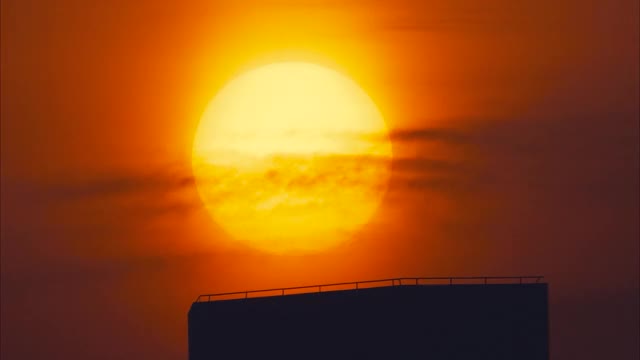 近距离的美丽的清晰的大日落，大红色的热太阳在温暖的空气扭曲落在城市建筑，时间流逝或快速运动镜头。视频素材