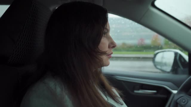 深褐色的女人，穿着大衣，坐在方向盘后面，在秋雨中驾驶汽车视频下载