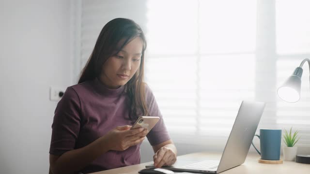 年轻的亚洲女性拿着纸账单，用她的智能手机在线支付视频素材