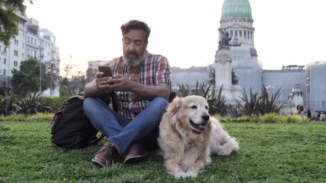 一个成熟的男人带着金毛猎犬在夕阳下的公园里散步，还在打电话视频下载