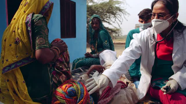 医务人员、医生、卫生保健工作者在大流行期间访问一户农村家庭，检查一名躺在床上、由其家人因疾病和年老而照顾的印度农村老年男性视频下载