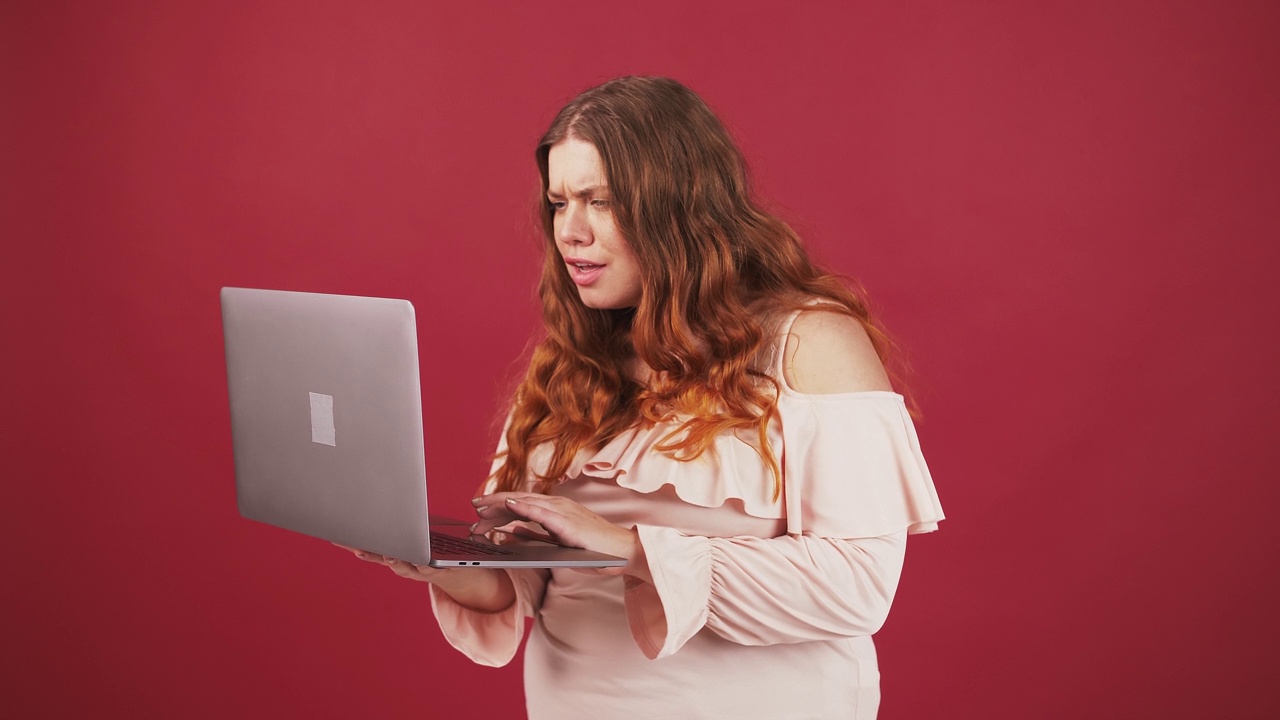 激动的胖女人看着笔记本电脑屏幕，兴奋地举起手，红色的画室背景视频素材
