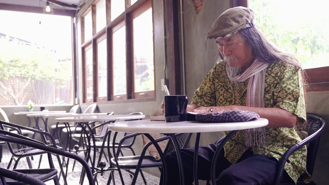 亚洲老人坐在咖啡厅用钢笔画画的肖像视频下载