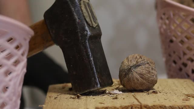 一个男人用锤子刺核桃。在一个木块上。切碎的坚果扔进篮子里。特写镜头。视频素材