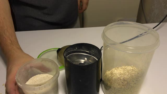 一个男人正在往咖啡研磨机里倒燕麦粥。把它们磨成面粉。视频下载