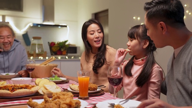 幸福的家庭时间和关系，亚洲大家庭有一个小聚会，一起在家里吃东西。爷爷很高兴看到他的孩子和侄子在家里的餐桌上吃饭，分享食物。视频下载