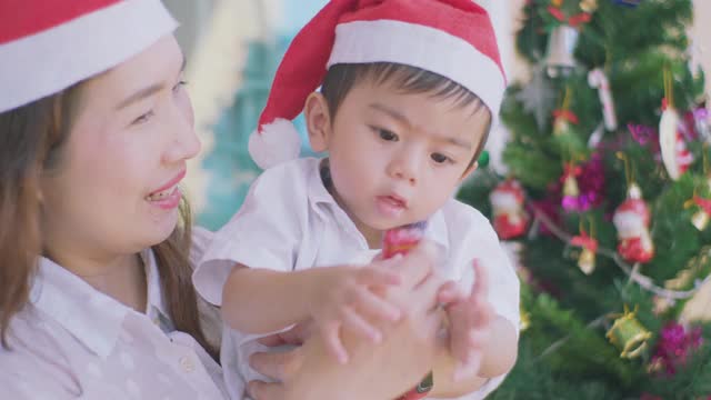 可爱的小男孩和妈妈看着圣诞树，寻找礼物。视频素材
