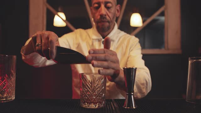 调酒师在鸡尾酒杯中加入冰块搅拌，在地下酒吧制作鸡尾酒视频下载