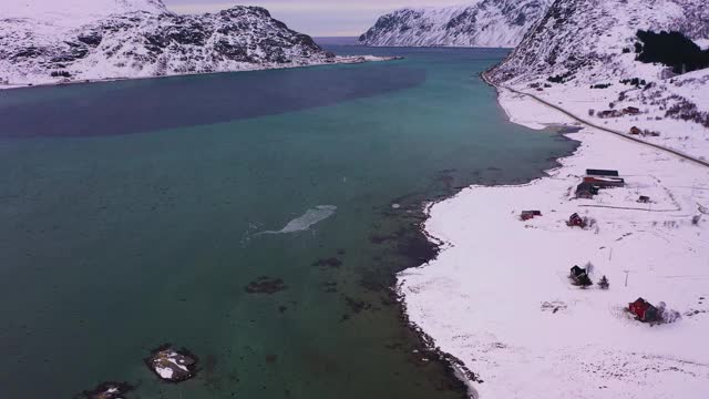 冬天的路，弗拉格斯塔德花粉和山脉。多云的天空。挪威罗浮敦群岛的Flakstadoya。鸟瞰图。无人机向前飞，向上倾斜。揭示拍摄视频素材