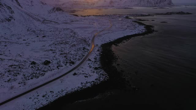 冬季日落时的路、海、岸、山。挪威罗浮敦群岛的Flakstadoya。鸟瞰图。无人机向前飞，向上倾斜。揭示拍摄视频素材