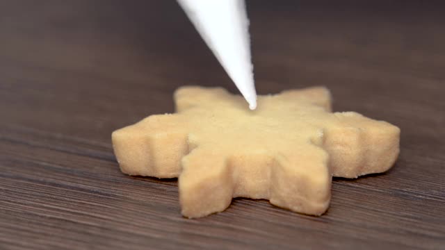 近距离绘制圣诞雪花糖饼干在木制桌子的背景与糖霜。视频素材