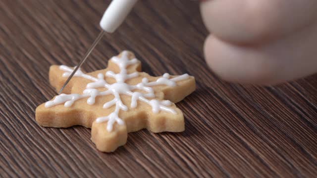 近距离绘制圣诞雪花糖饼干在木制桌子的背景与糖霜。视频素材
